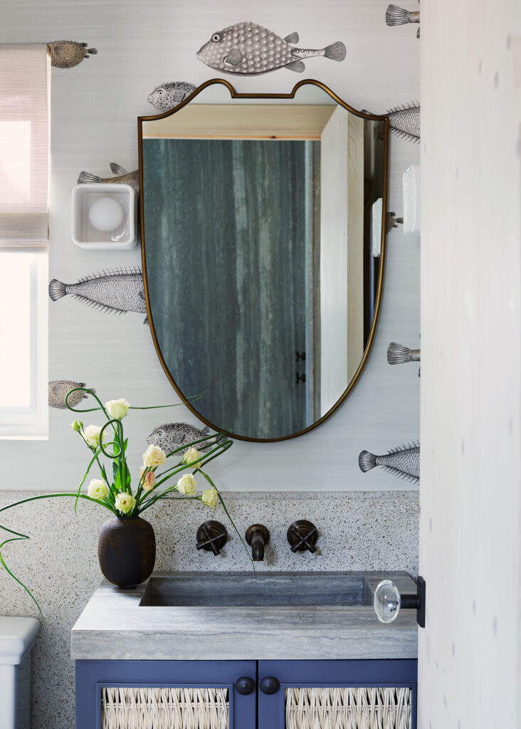 Modern coastal bathroom vanity with terrazzo countertop, brass mirror, and whimsical fish wallpaper showing sophisticated approach to marine-inspired interior design