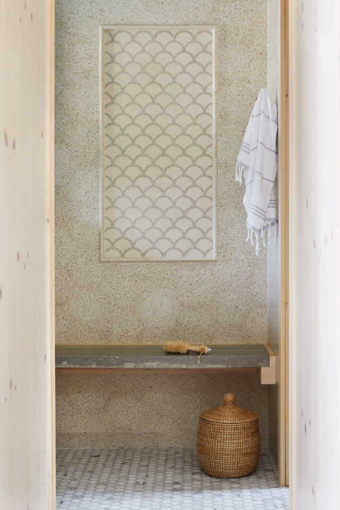 Spa bench area in coastal bathroom featuring scalloped wave pattern tile detail, terrazzo surfaces, and natural materials showing sophisticated marine references through form.