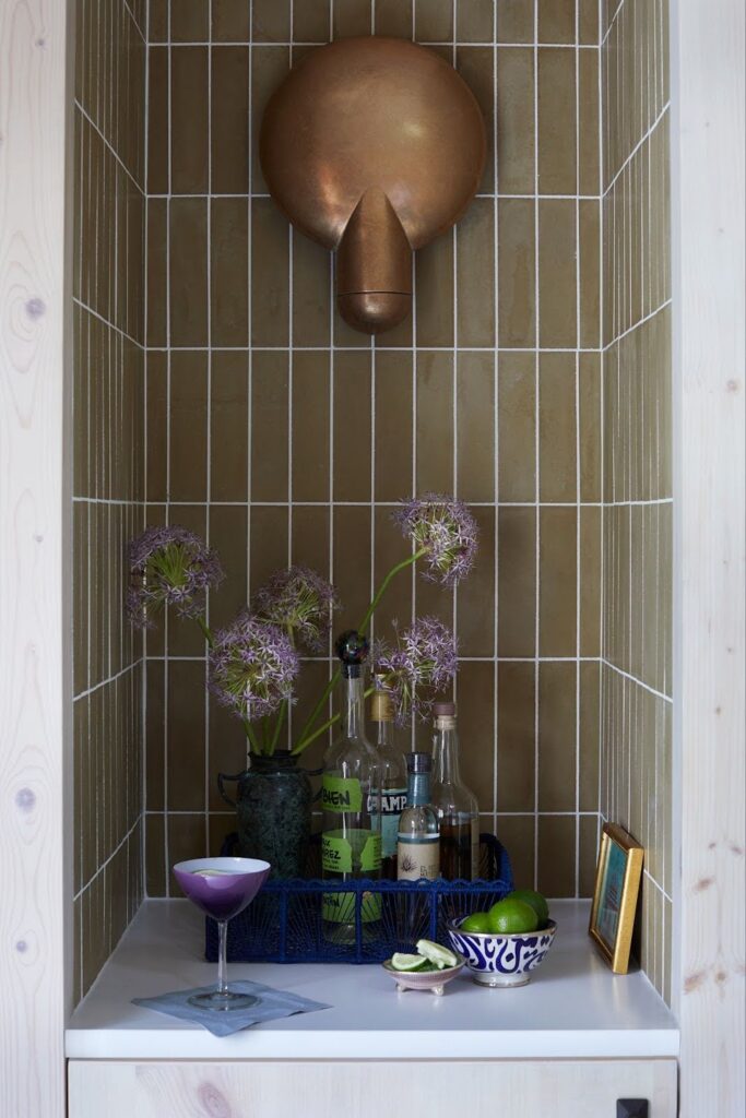 Recessed bar niche in Manasquan pool house with olive green stacked tile, sculptural brass sconce by Henry Wilson, whitewashed pine surround and styled bar accessories