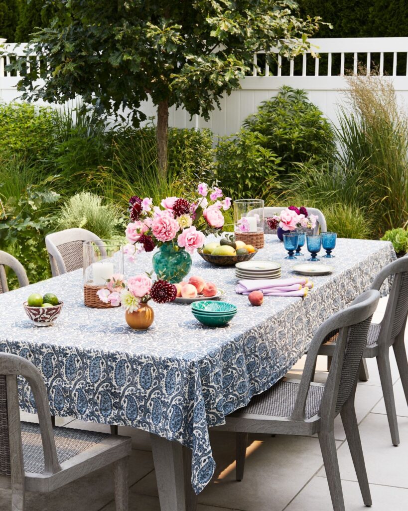 Blue and white paisley tablecloth set for outdoor entertaining with peonies dahlias and blue glassware on a shore home patio