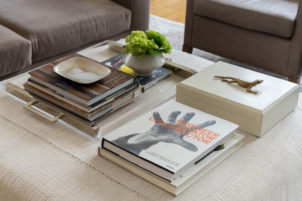 Lucite coffee table tray styled with a stack of art and design books topped by a MoMA monograph, a ceramic dish, a bronze lizard sculpture and a white lacquer box