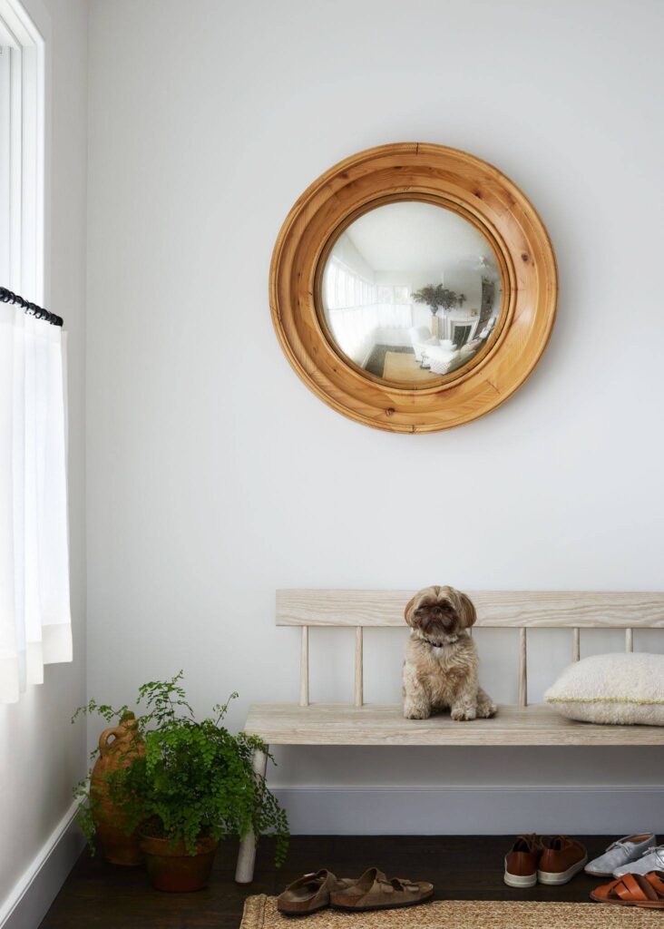 Wooden bench beneath a convex mirror with family dog Hermione seated, sandals lined up below in a coastal entryway