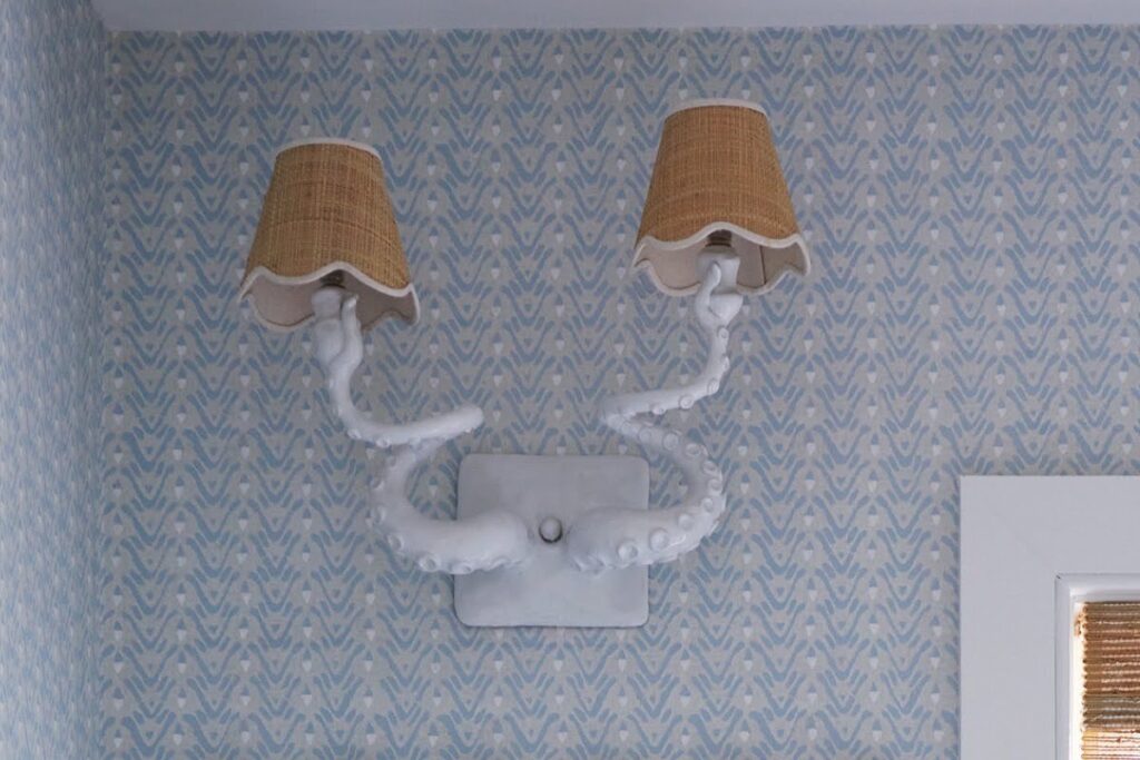 Custom white octopus sconce by Adam Wallacavage with scalloped rattan shades on blue patterned wallpaper.