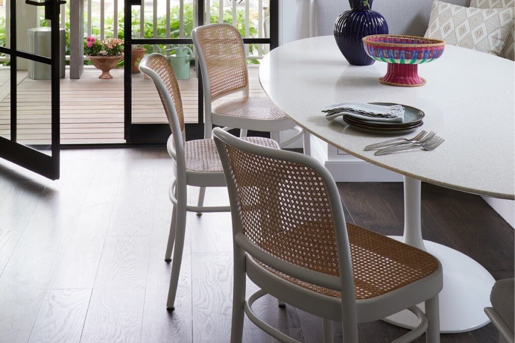 Oval terrazzo dining table by Robert Sukrachand with cane-back chairs and Atelier Domingue steel doors in Laura Krey Design's Manasquan home.